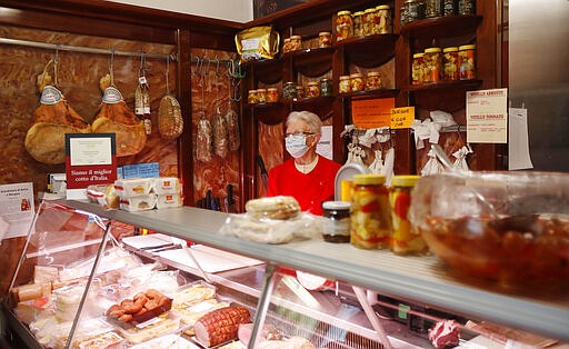 In this photo taken on Thursday, March 12, 2020, a shopkeeper wears a mask as she stands in her deli meat and cold cuts shop in Codogno, Italy. The northern Italian town that recorded Italy&#146;s first coronavirus infection has offered a virtuous example to fellow Italians, now facing an unprecedented nationwide lockdown, that by staying home, trends can reverse. Infections of the new virus have not stopped in Codogno, which still has registered the most of any of the 10 Lombardy towns Italy&#146;s original red zone, but they have slowed. For most people, the new coronavirus causes only mild or moderate symptoms. For some it can cause more severe illness. (AP Photo/Antonio Calanni)