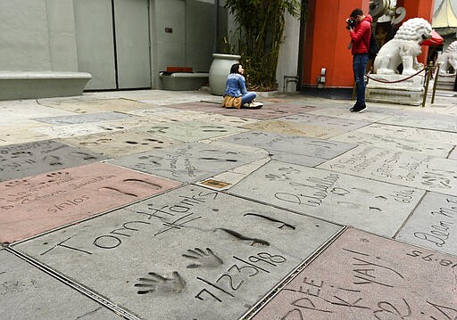 Visitors take pictures near the cement inscription of actor Tom Hanks in the forecourt of the TCL Chinese Theatre, Thursday, March 12, 2020, in the Hollywood section of Los Angeles. Hanks and his wife, actress-singer Rita Wilson, have tested positive for the coronavirus, the actor said in a statement Wednesday. For most people, the new coronavirus causes only mild or moderate symptoms. For some it can cause more severe illness.  (AP Photo/Chris Pizzello)