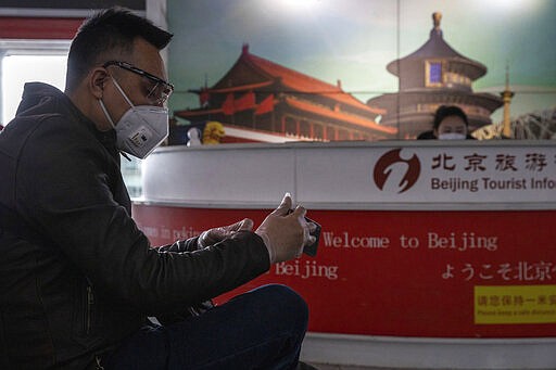 In this March 12, 2020, photo, a traveler waits near a tourist information booth at the Capital International Airport terminal 3 in Beijing. As the number of new cases dwindles in China and multiplies abroad, the country once feared as the source of the COVID-19 outbreak is now worried about importing cases from abroad. China hasn't imposed any travel bans, but Beijing said this week that all people arriving from overseas would have to self-quarantine for 14 days. (AP Photo/Ng Han Guan)