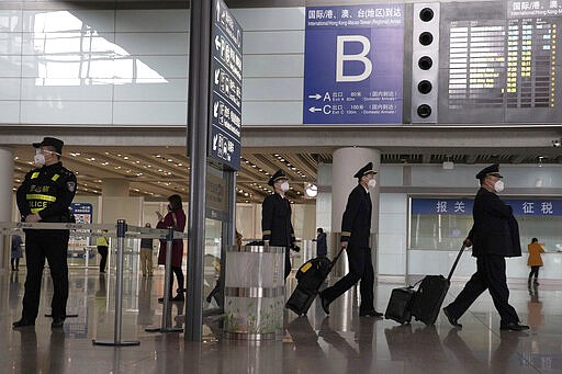 In this March 12, 2020, photo, air crew members walk past the international arrival exit at the Capital International Airport terminal 3 in Beijing. As the number of new cases dwindles in China and multiplies abroad, the country once feared as the source of the COVID-19 outbreak is now worried about importing cases from abroad. China hasn't imposed any travel bans, but Beijing said this week that all people arriving from overseas would have to self-quarantine for 14 days. (AP Photo/Ng Han Guan)