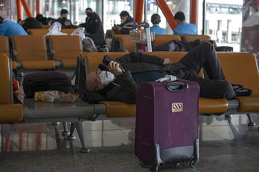 In this March 12, 2020, photo, a man wearing a mask rests on seats at the Capital International Airport terminal 3 in Beijing. As the number of new cases dwindles in China and multiplies abroad, the country once feared as the source of the COVID-19 outbreak is now worried about importing cases from abroad. China hasn't imposed any travel bans, but Beijing said this week that all people arriving from overseas would have to self-quarantine for 14 days. For most people, the new coronavirus causes only mild or moderate symptoms. (AP Photo/Ng Han Guan)