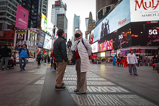 A pedestrian wearing a face mask stops in Times Square, Thursday, March 12, 2020, in New York. New York City Mayor Bill de Blasio said Thursday he will announce new restrictions on gatherings to halt the spread of the new coronavirus in the coming days. For most people, the new coronavirus causes only mild or moderate symptoms. For some it can cause more severe illness.  (AP Photo/John Minchillo)