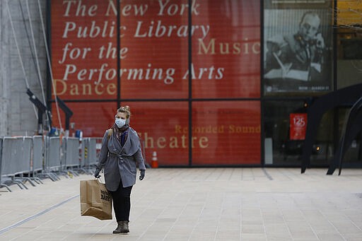 A mask-wearing woman walks in front of the New York Public Library for the Performing Arts at Lincoln Center, Thursday, March 12, 2020, in New York. Most of Lincoln Center's performance space including the Metropolitan Opera, shuttered their doors Thursday after New York Gov. Andrew Cuomo temporarily banned gatherings of more than 500 people amid a rise in cases of coronavirus. For most people the new virus causes only mild or moderate symptoms, such as fever and cough. For some, especially older adults and people with existing health problems, it can cause more severe illness including pneumonia. (AP Photo/Kathy Willens)