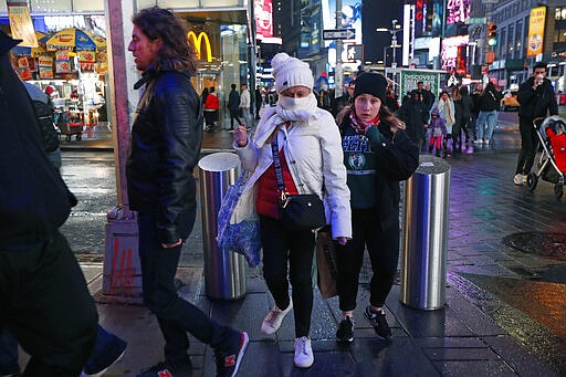 Tourists, including one using a scarf to protect her face against coronavirus in spite of relatively mild winter temperatures, walk through Times Square, Thursday, March 12, 2020, in New York. New York's Gov. Cuomo banned gatherings of more than 500 people in the city, forcing Broadway theaters and many city attractions to close. (AP Photo/Kathy Willens)