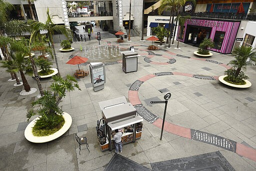 A vendor waits for customers in a sparsely populated courtyard at the Hollywood &amp; Highland shopping and entertainment complex, Thursday, March 12, 2020, in the Hollywood section of Los Angeles. (AP Photo/Chris Pizzello)