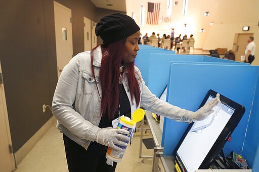 Denise Arnold, an early voting election official with the Chicago Board of Elections sanitizes a voting machine inside the Cook County Jail as eligible inmates participate in early voting for the March 17, Illinois primary, Saturday, March 14, 2020, in Chicago. (AP Photo/Charles Rex Arbogast)