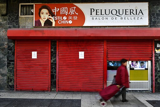 A woman walks past a Chinese hairdresser reading on top left ''Chinese Style'' and closed to prevent the spread of coronavirus in Vitoria, northern Spain, Saturday, March 14, 2020. Spain's prime minister has announced a two-week state of emergency from Saturday in a bid to contain the new coronavirus outbreak. For most people, the new COVID-19 coronavirus causes only mild or moderate symptoms, such as fever and cough, but for some, especially older adults and people with existing health problems, it can cause more severe illness, including pneumonia. (AP Photo/Alvaro Barrientos)