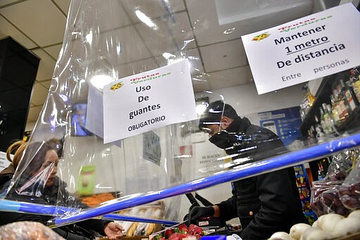 A vendor protects himself with a piece of plastic with signs reminding customers to keep their distance in Vitoria, northern Spain, Saturday, March 14, 2020. Spain's prime minister has announced a two-week state of emergency from Saturday in a bid to contain the new coronavirus outbreak. For most people, the new COVID-19 coronavirus causes only mild or moderate symptoms, such as fever and cough, but for some, especially older adults and people with existing health problems, it can cause more severe illness, including pneumonia. (AP Photo/Alvaro Barrientos)