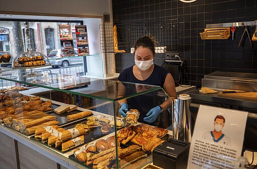 A woman wearing a mask serves sandwiches in a bar in Barcelona, Spain, Saturday, March 14, 2020. Spain's prime minister has announced a two-week state of emergency from Saturday in a bid to contain the new coronavirus outbreak. For most people, the new coronavirus causes only mild or moderate symptoms. For some, it can cause more severe illness, especially in older adults and people with existing health problems. (AP Photo/Emilio Morenatti)