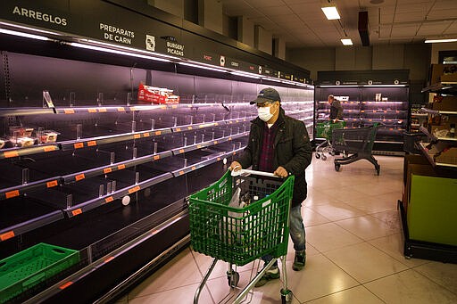 A man wearing a mask walks past empty shelves in a meat market in Barcelona, Spain, Saturday, March 14, 2020. Spain's prime minister has announced a two-week state of emergency from Saturday in a bid to contain the new coronavirus outbreak. For most people, the new coronavirus causes only mild or moderate symptoms. For some, it can cause more severe illness, especially in older adults and people with existing health problems. (AP Photo/Emilio Morenatti)