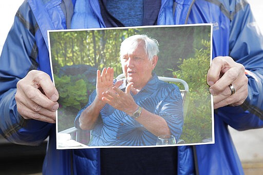 In this March 12, 2020, photo, Scott Sedlacek poses for a photo while holding a picture of his father, Chuck, outside Life Care Center in Kirkland, Wash., near Seattle. The facility has been at the center of the COVID-19 coronavirus outbreak in the state, and Sedlacek &#151; who also has tested positive for the virus &#151; said he and his siblings have barely spoken to their father, who in addition to testing positive for the coronavirus, has blindness, neuropathy, and has difficulty using a phone, saying he is more of an &quot;inmate&quot; than a patient. Residents of assisted living facilities and their loved ones are facing a grim situation as the coronavirus spreads across the country, placing elderly people especially at risk. (AP Photo/Ted S. Warren)