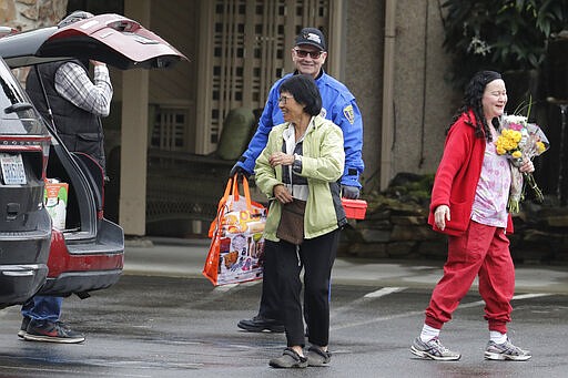 In this March 6, 2020, photo, Su Wilson, front left, smiles after giving a worker at Life Care Center in Kirkland, Wash., flowers to give to her mother, June Liu, who lives at the facility, which has been at the center of the COVID-19 coronavirus outbreak in the state. Residents of assisted living facilities and their loved ones are facing a grim situation as the coronavirus spreads across the country, placing elderly people especially at risk. (AP Photo/Ted S. Warren)