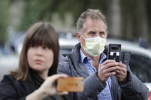 In this March 11, 2020, photo, Scott Sedlacek, right, who has tested positive for the COVID-19 coronavirus, wears a mask as he stands near reporters and listens to a spokesman for Life Care Center in Kirkland, Wash., during a daily press briefing. Sedlacek's father, Chuck, who also has tested positive, lives in the facility, which has been at the center of the COVID-19 coronavirus outbreak in the state, and Sedlacek said he and his siblings have barely spoken to their father, who has blindness and neuropathy, and difficulty using a phone, saying he is more of an &quot;inmate&quot; than a patient. Residents of assisted living facilities and their loved ones are facing a grim situation as the coronavirus spreads across the country, placing elderly people especially at risk. (AP Photo/Ted S. Warren)