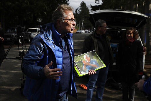 In this March 12, 2020 photo, Scott Sedlacek becomes animated as he holds a picture of his father, Chuck, and talks to reporters outside Life Care Center in Kirkland, Wash., near Seattle. The facility has been at the center of the COVID-19 coronavirus outbreak in the state, and Sedlacek &#151; who also has tested positive for the virus &#151; said he and his siblings have barely spoken to their father who lives inside the center, and in addition to testing positive for the coronavirus, has blindness, neuropathy, and has difficulty using a phone, saying he is more of an &quot;inmate&quot; than a patient. Residents of assisted living facilities and their loved ones are facing a grim situation as the coronavirus spreads across the country, placing elderly people especially at risk. (AP Photo/Ted S. Warren)