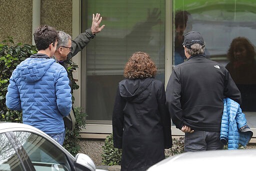 In this March 12, 2020, photo, family members of Chuck Sedlacek wave and greet him through reflections in the window of his room at Life Care Center in Kirkland, Wash., near Seattle. The facility has been at the center of the COVID-19 coronavirus outbreak in the state, and Sedlacek's son Scott said that he and his siblings have barely spoken to their father inside the center, who in addition to testing positive for the coronavirus, has blindness, neuropathy, and has difficulty using a phone, saying he is more of an &quot;inmate&quot; than a patient. Residents of assisted living facilities and their loved ones are facing a grim situation as the coronavirus spreads across the country, placing elderly people especially at risk. (AP Photo/Ted S. Warren)