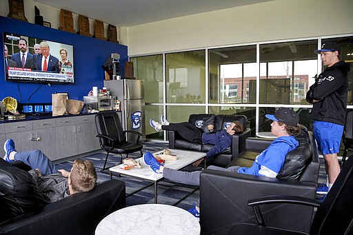 In this March 13, 2020 photo, Creighton NCAA college baseball pitchers Ben Dotzler, right, and Tommy Steier, second right, watch President Trump declare a national emergency to combat the coronavirus pandemic, in the player lounge in Omaha, Neb.. Dotzler was supposed to be in the bullpen at TD Ameritrade Park this weekend readying himself to pitch against Northern Colorado, Everything changed for hm and thousands of other college athletes when the NCAA announced March 12, 2020, it was canceling all spring sports championships, along with remaining winter championships, as a precaution against the spread of the new coronavirus.  (AP Photo/Nati Harnik)