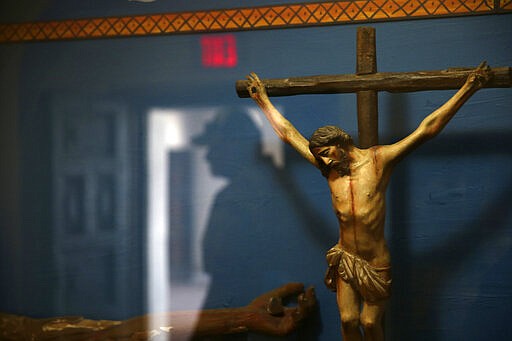 A man is reflected in a glass case containing a statue of a crucified Jesus Christ at the museum of the Mission San Xavier del Bac in Tucson, Ariz., Friday, Feb. 21, 2020. San Xavier was founded as a Catholic mission by Father Eusebio Kino in 1692 when Southern Arizona was part of New Spain. (AP Photo/Dario Lopez-MIlls)