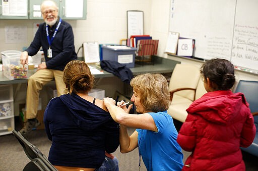 Volunteers give flu shots to newly arrived asylum seekers from Central America at Casa Alitas, a Catholic-run shelter in Tucson, Ariz., Friday, Feb. 21, 2020. In numerous cities along the border with Mexico, Catholic-run agencies are outspoken advocates for migrants and asylum seekers hoping to reach the U.S. (AP Photo/Dario Lopez-MIlls)