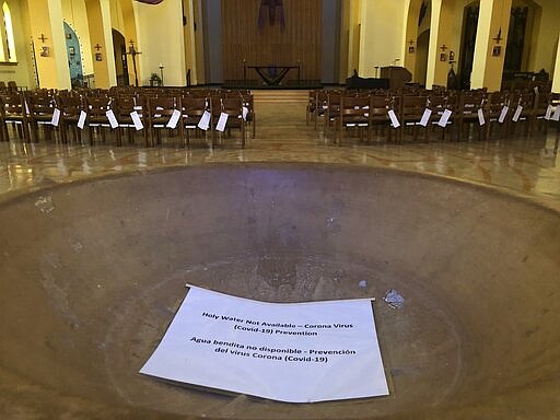 In this Saturday, March 14, 2020 photo, a sign reads, &quot;Holy Water Not Available&quot; in the baptismal font of the St. Stephen and the Incarnation Episcopal Church in Washington, which is closed due to the coronavirus pandemic. (AP Photo/Federica Narancio)