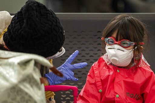 A woman plays with her daughter as they wait at Barcelona airport, Spain, Saturday, March 14, 2020. Spain's prime minister has announced a two-week state of emergency from Saturday in a bid to contain the new coronavirus outbreak. For most people, the new coronavirus causes only mild or moderate symptoms. For some, it can cause more severe illness, especially in older adults and people with existing health problems. (AP Photo/Emilio Morenatti)