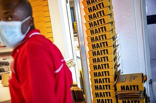 Boxes of rum are stacked as a duty free employee wears a mask while working at Toussaint Louverture International Airport, Saturday, March 14, 2020, in Port-au-Prince, Haiti.   As of Saturday, Haiti has no reported cases of COVID-19 coronavirus.  For most people, the new coronavirus causes only mild or moderate symptoms. For some it can cause more severe illness. (AP Photo/David Goldman)