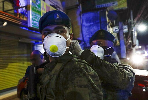 A Filipino army trooper helps his comrade wear a protective masks as they arrive to augment police at Valenzuela, metropolitan Manila, Philippines early Sunday March 15, 2020. Thousands of Philippine police, backed by the army and coast guard, have started sealing the densely populated capital from most domestic travelers in one of Southeast Asia's most drastic containment moves against the coronavirus. For most people, the new coronavirus causes only mild or moderate symptoms. For some, it can cause more severe illness, especially in older adults and people with existing health problems. (AP Photo/Aaron Favila)