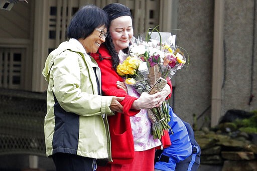 In this March 6, 2020, photo, Su Wilson, left, takes a photo with a worker at Life Care Center in Kirkland, Wash., after handing off flowers to give to her mother, June Liu, who lives at the facility, which has been at the center of the COVID-19 coronavirus outbreak in the state. Residents of assisted living facilities and their loved ones are facing a grim situation as the coronavirus spreads across the country, placing elderly people especially at risk. (AP Photo/Ted S. Warren)