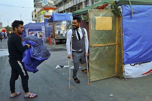 In this Saturday, March 7, 2020 photo, a protester holds a cover for his tent in Tahrir Square, Baghdad, Iraq. Where once the square had seen thousands every day, now only a few hundred protesters turn up. The youthful protesters are struggling to keep their movement going after one set-back after another, now capped by fears over the virus outbreak. For most people, the virus causes only mild or moderate symptoms. For some it can cause more severe illness. (AP Photo/Hadi Mizban)