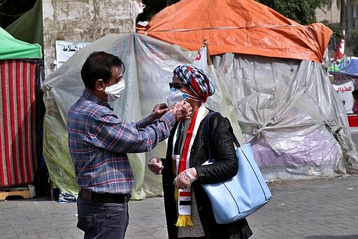 In this Sunday, March 8, 2020 photo, protesters help each other adjust face masks against the new coronavirus, during a sit-in at Tahrir Square in Baghdad, Iraq. Where once the square had seen thousands every day, now only a few hundred protesters turn up. The youthful protesters are struggling to keep their movement going after one set-back after another, now capped by fears over the virus outbreak. For most people, the virus causes only mild or moderate symptoms. For some it can cause more severe illness. (AP Photo/Khalid Mohammed)