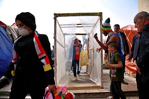 In this Sunday, March 8, 2020 photo, anti-government protesters enter a makeshift disinfecting booth set up by the protesters to help protect against the spread of the new coronavirus, in Baghdad, Iraq. Where once Baghdad&#146;s Tahrir Square had seen thousands every day, now only a few hundred protesters turn up. The youthful protesters are struggling to keep their movement going after one set-back after another, now capped by fears over the virus outbreak. For most people, the virus causes only mild or moderate symptoms. For some it can cause more severe illness. (AP Photo/Khalid Mohammed)