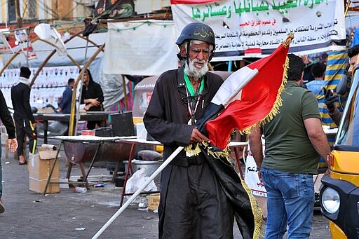 In this Saturday, March 7, 2020 photo, a protester holds an Iraqi flag, in Tahrir Square, Baghdad, Iraq. Where once the square had seen thousands every day, now only a few hundred protesters turn up. The protesters are struggling to keep their movement going after one set-back after another, now capped by fears over the virus outbreak. For most people, the virus causes only mild or moderate symptoms. For some it can cause more severe illness. (AP Photo/Hadi Mizban)