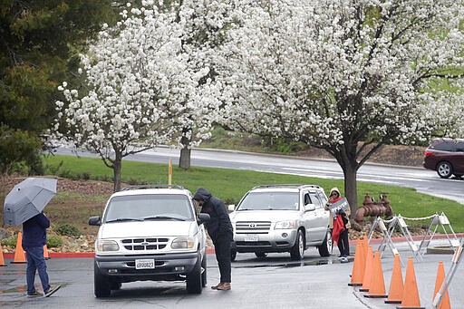 Executive pastor Jason Bishop, center, and Leona Njoku-Obi, right, talks to drivers in cars while offering drive up prayer service outside of The Bay Church in Concord, Calif., Sunday, March 15, 2020. (AP Photo/Jeff Chiu)