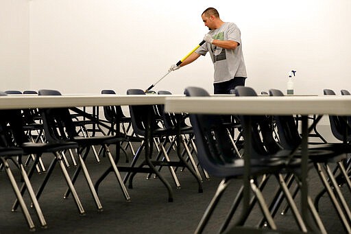 Grace Bible Church facilities manager Kenny Sitton sanitizes classroom tables at the church Friday, March 13, 2020, in Tempe, Ariz. after church leaders participated in a state-wide conference call with Arizona Disease Control that highlighted the state's guidelines for preventing the spread of COVID-19 coronavirus in houses of worship. The church stated that morning Services are currently scheduled to continue with the exceptions of canceled child care, reconfigured seating to promote social distancing and gloved-greeters who will open and close doors for service attenders. (AP Photo/Matt York)