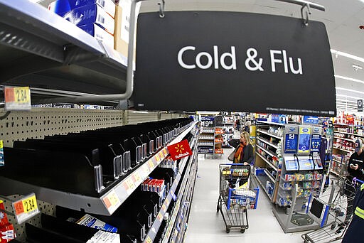 FILE - In this Friday, March 13, 2020, file photo, a woman looks at the few selections remaining in the cold and flu aisle of a Walmart near Warrendale, Pa. Walmart, the nation&#146;s largest retailer and private employer, said late Saturday, March 14, 2020, it is limiting store hours to ensure they can keep sought-after items such as hand sanitizer in stock amid the coronavirus pandemic. (AP Photo/Gene J. Puskar, File)