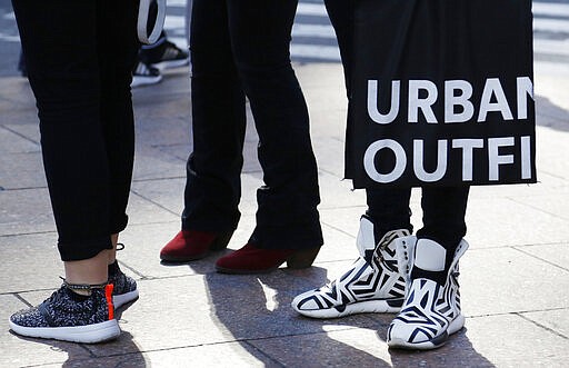 FILE - In this Wednesday, March 9, 2016, file photo, a man carries a shopping bag from Urban Outfitters, in New York. A growing list of retailers are closing stores or limiting their operating hours as customers remain home in an effort to slow the spread of the virus outbreak. Other retailers are following Apple and closing their stores, including Urban Outfitters, Everlane and Patagonia. (AP Photo/Mark Lennihan, File)