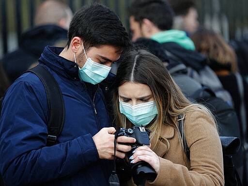 A couple wearing face masks to protect against the Coronavirus outbreak as they look at their photographs after visiting Buckingham Palace in London, Saturday, March 14, 2020. For most people, the new coronavirus causes only mild or moderate symptoms, such as fever and cough. For some, especially older adults and people with existing health problems, it can cause more severe illness, including pneumonia. (AP Photo/Frank Augstein)