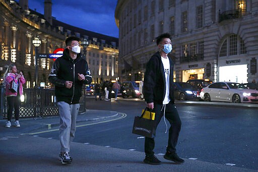 Two pedestrians cross the street wearing masks in Piccadilly Circus, London, Saturday, March 14, 2020. British Prime Minister Boris Johnson has described the worldwide pandemic as &#147;the worst public health crisis for a generation.&#148; (Hollie Adams/PA via AP)