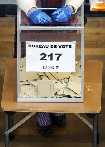 A volunteer using gloves waits for people in a polling station during local elections in Lyon, central France, Sunday, March 15, 2020. France is holding nationwide elections Sunday to choose all of its mayors and other local leaders despite a crackdown on public gatherings because of the new virus. For most people, the new coronavirus causes only mild or moderate symptoms. For some it can cause more severe illness. (AP Photo/Laurent Cipriani)