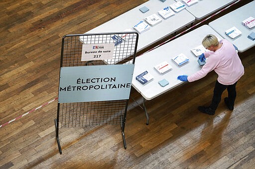 A volunteer cleans the table where the ballots are displayed for local elections in Lyon, central France, Sunday, March 15, 2020. France is holding nationwide elections Sunday to choose all of its mayors and other local leaders despite a crackdown on public gatherings because of the new virus. For most people, the new coronavirus causes only mild or moderate symptoms. For some it can cause more severe illness. (AP Photo/Laurent Cipriani)