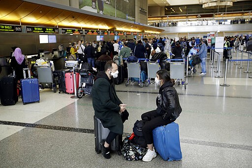 FILE - In this Saturday, March 14, 2020 file photo, travelers wait to check in their luggage at the Los Angeles International Airport. The coronavirus pandemic that's caused many Americans to avoid airports has others booking spur-of-the moment trips at dirt-cheap ticket prices. (AP Photo/Marcio Jose Sanchez, File)