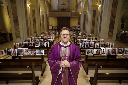 Robbiano Church parson, Don Giuseppe Corbari, poses in front of selfies he was sent by parishioners as Masses for the faithful have been suspended following Italy's coronavirus emergency, in Giussano, northern Italy, Sunday, March 15, 2020.  For most people, the new coronavirus causes only mild or moderate symptoms. For some, it can cause more severe illness, especially in older adults and people with existing health problems. (AP Photo/Luca Bruno)