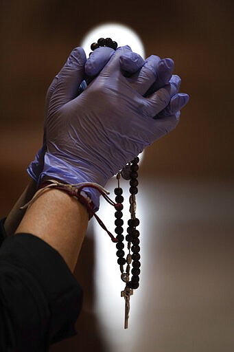 A Catholic worshipper using protective gloves prays with a rosary beads at the Santa Maria de Cana parish in Pozuelo de Alarcon, outskirts Madrid, Spain, Sunday, March 15, 2020. Pope Francis has praised people for their continuing efforts to help vulnerable communities, including the poor and the homeless, amid the coronavirus pandemic. The vast majority of people recover from the COVID-19. According to the World Health Organization, most people recover in about two to six weeks, depending on the severity of the illness. (AP Photo/Bernat Armangue)