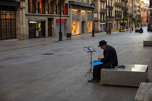 A man sits, in an empty street in Barcelona, Spain, Sunday, March 15, 2020. Spain's government announced Saturday that it is placing tight restrictions on movements and closing restaurants and other establishments in the nation of 46 million people as part of a two-week state of emergency to fight the sharp rise in coronavirus infections. For most people, the new coronavirus causes only mild or moderate symptoms. For some, it can cause more severe illness, especially in older adults and people with existing health problems. (AP Photo/Emilio Morenatti)