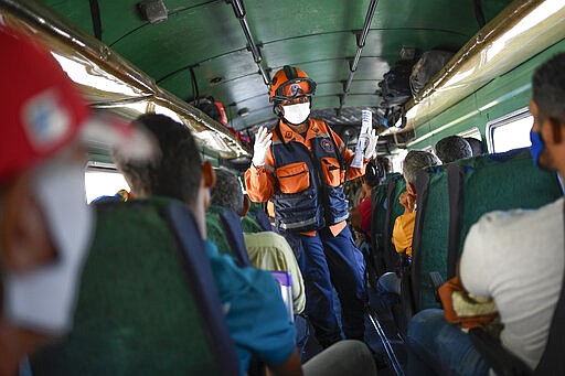 A member of the Venezuelan civil protection agency explains commuters symptoms and preventive measures for the new coronavirus in Caracas, Venezuela, Sunday, March 15, 2020. The vast majority of people recover from the new virus. (AP Photo/Matias Delacroix)