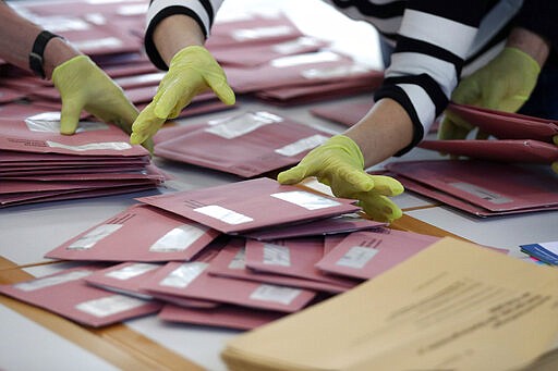 Volunteer wear gloves preparing postal votes in Munich, Germany, Sunday, March 15, 2020. Germany has been slower than some of its neighbours to ban large gatherings, initially leaving the decision to local authorities as required by country's federal structure. For some, especially older adults and people with existing health problems, it can cause more severe illness, including pneumonia. (AP Photo/Matthias Schrader)