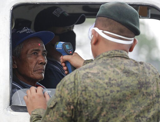 A man's temperature is checked by an army trooper before entering the metropolis at a checkpoint on the outskirts of Quezon city, Philippines Sunday, March 15, 2020. Thousands of Philippine police, backed by the army and coast guard, have started sealing the densely populated capital from most domestic travelers in one of Southeast Asia's most drastic containment moves against the coronavirus. For most people, the new coronavirus causes only mild or moderate symptoms. For some, it can cause more severe illness, especially in older adults and people with existing health problems. (AP Photo/Aaron Favila)