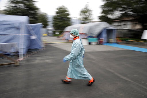 FILE - In this Thursday, March 12, 2020 file photo, a worker wearing a mask and protective clothing walks between the emergency structures that were set up to ease procedures at the Brescia hospital in northern Italy. The medical impact of the new coronavirus is coming into sharper focus in March 2020 as it continues its spread in what is now officially recognized as a pandemic. (AP Photo/Luca Bruno)