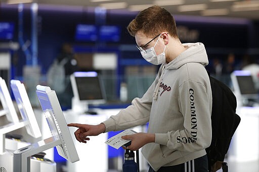 New York University student Hector Medrano, of Los Angeles, checks in for his flight using a touchscreen Saturday, March 14, 2020, at jetBlue's terminal in John F. Kennedy International Airport in New York. Medrano is traveling home during the school's spring break, and opted to wear a face mask as he travels to protect himself. (AP Photo/Kathy Willens)