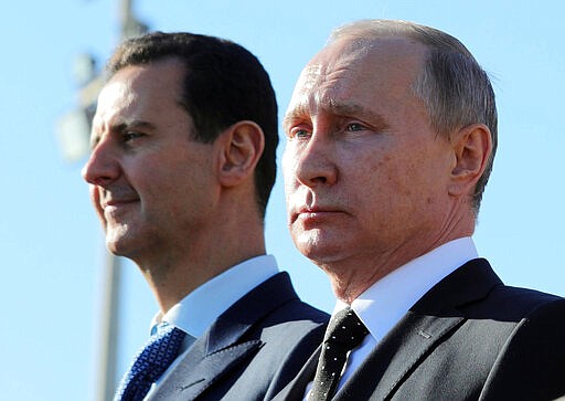 FILE - This Dec. 11, 2017 file photo, shows Russian President Vladimir Putin, right, and Syrian President Bashar Assad watching troops march at the Hemeimeem air base in Syria. In a world gripped by a pandemic, global unrest and a fast-moving news cycle, it can be difficult to remember that the war in Syria is still happening. (Mikhail Klimentyev, Sputnik, Kremlin Pool Photo via AP, File)