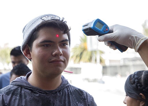 A health worker measures the temperature of a music fan as a precaution against the spread of the new coronavirus, at the entrance gates of the venue for the Vive Latino Music Festival, in Mexico City, Saturday, March 14, 2020. On Friday afternoon organizers confirmed that the 21st edition of the festival will go on as planned. However, preventive measures will be taken, such as checking the temperature of the attendees upon admission and providing antibacterial gel. (AP Photo/Christian Palma)